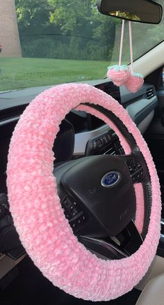 the steering wheel cover is pink and has fuzzy yarn on it, while hanging from a car's dashboard