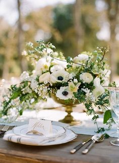 an arrangement of white flowers and greenery on a table