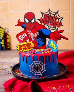 a spiderman birthday cake with sprinkles and decorations on the top, sitting on a table