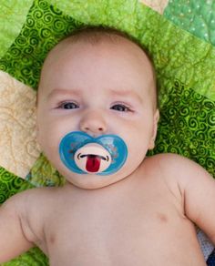 a baby with a pacifier on it's face laying on a green quilt