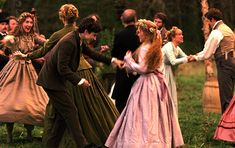 a group of people dressed in period clothing dancing on the grass with trees in the background