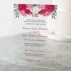 a clear acrylic card with pink roses and greenery on the bottom, in front of a wedding cake