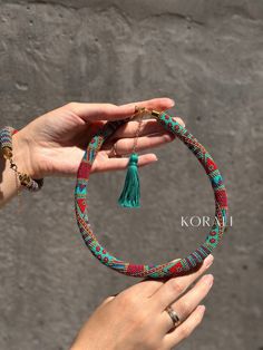 two hands holding a colorful bracelet with tassels