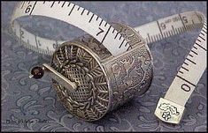 a measuring tape and an old silver thimble are on a blue background with ornate designs