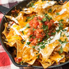 nachos in a cast iron skillet topped with salsa and sour cream sauce