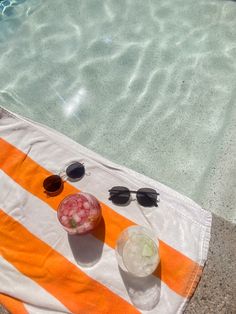 an orange and white beach towel with sunglasses on it next to a swimming pool filled with water