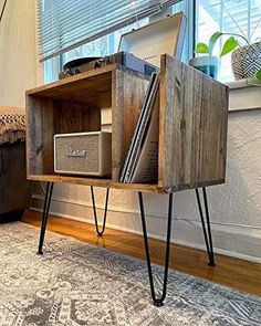 an old record player is sitting on a wooden stand next to a window with blinds