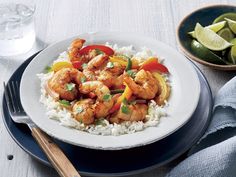 a white plate topped with shrimp and rice next to a bowl of lime wedges