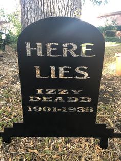 a black tombstone with the words here lies on it in front of a tree and grass