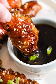 someone dipping sauce on top of chicken wings in a white bowl with sesame seed sprinkles