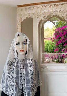 a mannequin wearing a veil and headpiece in front of a window with pink flowers