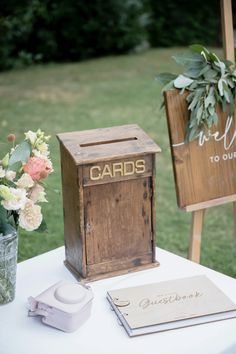 a wooden card box sitting on top of a table next to a vase filled with flowers