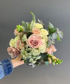 a person holding a bouquet of flowers in their left hand, against a gray background