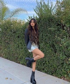 a woman in short shorts and jacket posing for the camera with her legs crossed, wearing high heeled boots