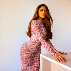 a woman in a pink and white dress leaning on a counter