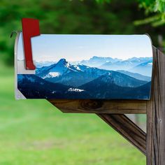 a mailbox with mountains in the background on a wooden post near some grass and trees