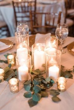 candles and greenery are arranged on the table for an elegant centerpiece at this wedding reception