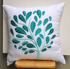 a white pillow with green leaves on it sitting on a wooden shelf next to a wall