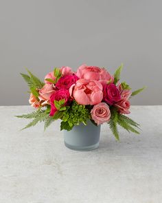 a vase filled with pink and red flowers on top of a white countertop next to a gray wall