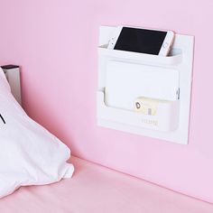 there is a phone charging station on the wall next to a bed with pink walls