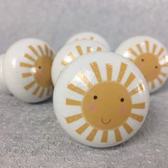 three yellow and white ceramic knobs with smiling sun faces on them, sitting on a gray surface