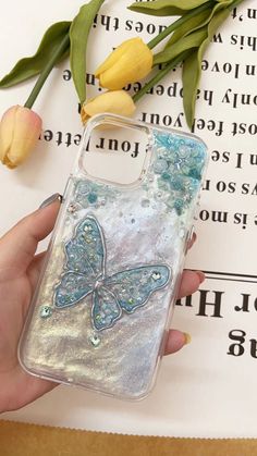 a hand holding an iphone case with a butterfly on it and flowers in the background