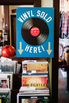 there is a sign that says vinyl sold here and many records are stacked on the table