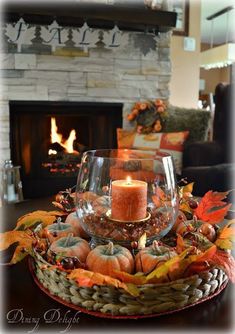 a candle is lit in a glass bowl filled with autumn leaves and pumpkins on a table