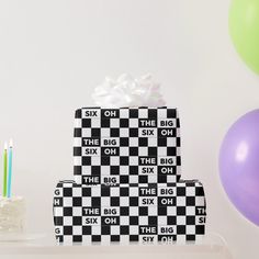 three black and white gift boxes with candles on the top, next to some balloons