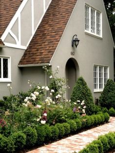 a gray house with white trim and brown shingles on the roof is surrounded by greenery