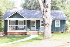 a small blue house with porches and trees in the front yard on a sunny day