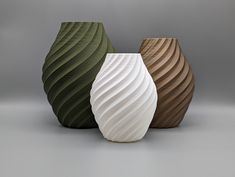 three different colored vases sitting next to each other on a gray surface, one with wavy lines