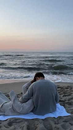 a man sitting on top of a towel next to the ocean under a pink sky