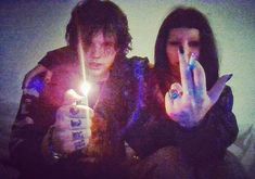 two people sitting next to each other holding candles in front of their faces and making the peace sign