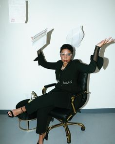 a woman sitting in a chair with her hands up and papers flying above her head