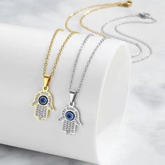 Featuring a delicate Hamsa Hand pendant adorned with sparkling cubic zirconia stones and a captivating evil eye, this necklace is a symbol of good luck, health, and happiness.  What's Included: 1 x Necklace or Necklace Set of 2 Pendant Size: 1cmx1.5cm Key Features: *Symbolic Design: Combines the protective power of the Hamsa Hand and Evil Eye *Sparkling Cubic Zirconia: Adds a touch of glamour and elegance *Gold/Silver Finish: Choose the perfect metal to match your style *Delicate Chain: Creates Silver Cubic Zirconia Charm Necklaces, Tarnish Resistant, Silver Tarnish Resistant Charm Necklaces With Cubic Zirconia, Silver Spiritual Necklace With Cubic Zirconia, Spiritual Silver Cubic Zirconia Necklace, Spiritual Silver Necklace With Cubic Zirconia, Silver Cubic Zirconia Charm Necklaces For Jewelry Making, Silver Metal Jewelry With Evil Eye, Silver Metal Evil Eye Jewelry, Durable Silver Crystal Jewelry