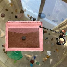 a pink and brown card case hanging from a metal chain on a glass table with rocks in the background