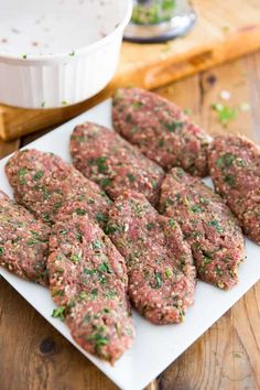 some meat patties are on a white plate next to a bowl and cutting board