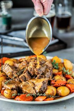 a person pouring sauce on top of some meat and potatoes in a white plate with carrots