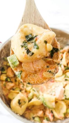 a wooden spoon full of pasta with spinach and cheese on it, being lifted from a casserole dish