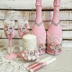 three pink wine bottles are sitting next to two champagne glasses and a candle holder with flowers on them