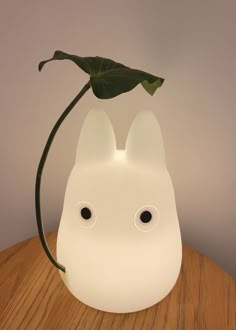 a white cat lamp with a green plant in the shape of a face on top of a wooden table