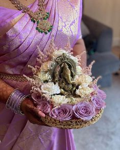 a woman in a purple sari holding a basket with flowers and an idol on it