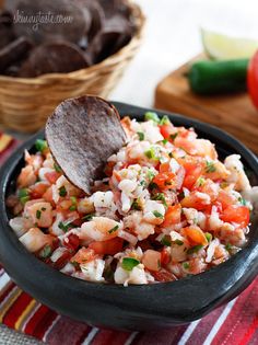 a black bowl filled with rice and vegetables next to a tortilla shell on a striped towel