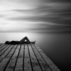 black and white photograph of a person laying down on a dock with the ocean in the background