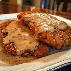 some type of meat with gravy on top of it sitting on a plate