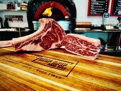 two raw meats sitting on top of a wooden cutting board in front of an oven