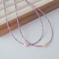 two necklaces with pearls on them sitting next to a piece of wood and window sill