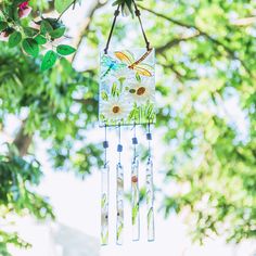 a wind chime hanging from a tree branch with flowers and leaves in the background