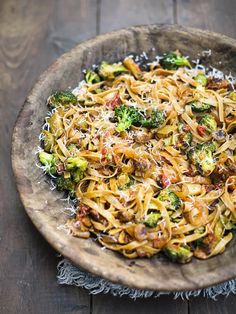 a wooden bowl filled with pasta and broccoli on top of a wood table